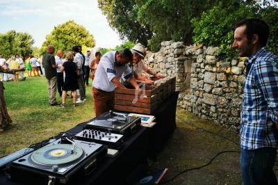 Des personnes participent à une activité en plein air près d'une table de disques vinyles et d'un mur en pierre.