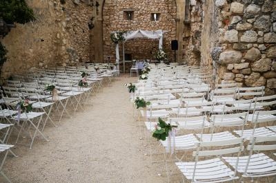 Chaises blanches alignées face à une arche en pierre décorée pour une cérémonie dans une ruine historique en plein air.