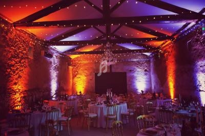 Salle de réception décorée avec des tables rondes, éclairage coloré et guirlandes lumineuses suspendues.
