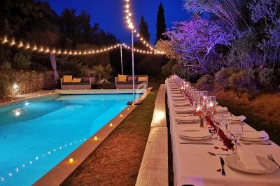 Table dressée avec des bougies et pétales de rose près d'une piscine éclairée, entourée de guirlandes lumineuses et…