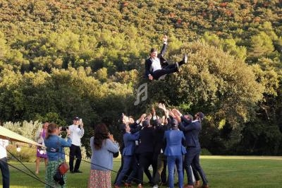 Un groupe d'hommes en costume lance un autre homme en l'air lors d'une célébration en plein air devant une forêt.