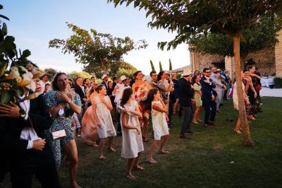 Groupe de personnes dansant en extérieur sur une pelouse, entouré d'arbres et d'un bâtiment en pierre.