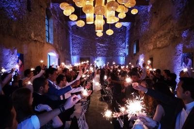 Des invités brandissent des cierges magiques dans une salle en pierre illuminée pour une célébration festive.