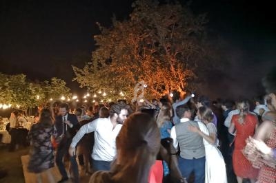 Groupe de personnes dansant en plein air la nuit, éclairé par des guirlandes lumineuses et un arbre illuminé.