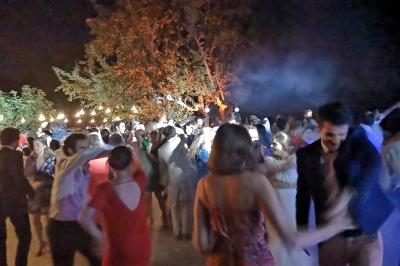 Des personnes dansent en soirée en plein air, éclairées par des guirlandes lumineuses et des projecteurs.