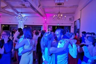 Des couples dansent dans une salle éclairée par des lumières colorées, avec des poutres apparentes et des lustres.