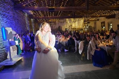 Une mariée danse avec un invité dans une salle en pierre décorée de guirlandes lumineuses, entourée de convives.