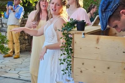 Une femme en robe blanche, entourée de convives, près d'un buffet en extérieur lors d'une réception.