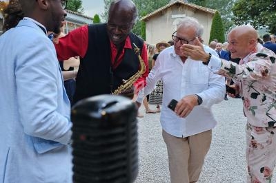 Des personnes discutent et rient dans une ambiance festive en extérieur, avec un micro visible au premier plan.