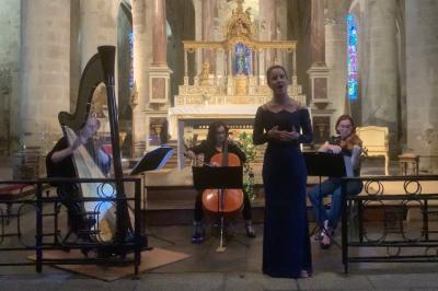 Une violoncelliste joue lors d'une cérémonie dans une église, entourée d'invités debout et de mariés à l'arrière-plan.