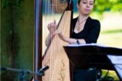 Une violoncelliste joue lors d'une cérémonie dans une église, entourée d'invités debout et de mariés à l'arrière-plan.