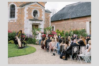 Une violoncelliste joue lors d'une cérémonie dans une église, entourée d'invités debout et de mariés à l'arrière-plan.