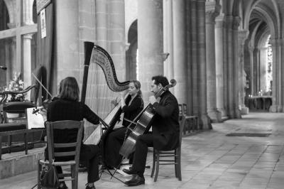 Une violoncelliste joue lors d'une cérémonie dans une église, entourée d'invités debout et de mariés à l'arrière-plan.