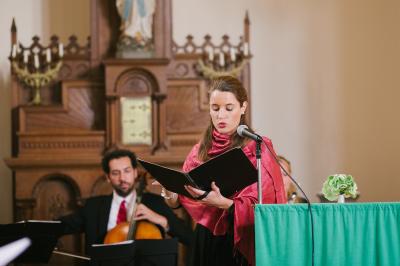 Une violoncelliste joue lors d'une cérémonie dans une église, entourée d'invités debout et de mariés à l'arrière-plan.