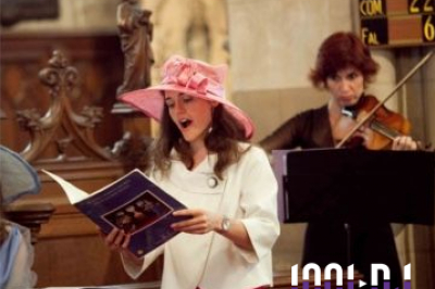 Une violoncelliste joue lors d'une cérémonie dans une église, entourée d'invités debout et de mariés à l'arrière-plan.