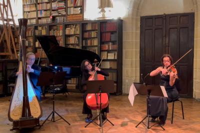 Une violoncelliste joue lors d'une cérémonie dans une église, entourée d'invités debout et de mariés à l'arrière-plan.