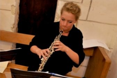 Une violoncelliste joue lors d'une cérémonie dans une église, entourée d'invités debout et de mariés à l'arrière-plan.