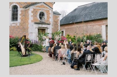 Cérémonie de mariage en plein air devant une chapelle en briques, avec invités assis et une harpiste jouant.