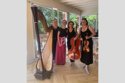 Quatre musiciennes posent avec une harpe, un violoncelle et un violon dans une pièce lumineuse avec parquet en bois.
