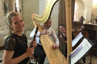 Trois musiciens jouent de la harpe, du violoncelle et de la clarinette dans un intérieur en pierre lumineuse.