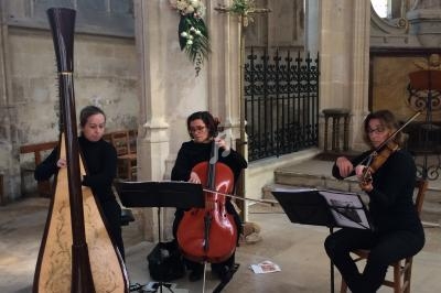 Trois musiciennes jouent de la harpe, du violoncelle et du violon dans une église lumineuse.