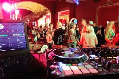 Vue d'une soirée dansante avec une table de mixage et un ordinateur au premier plan, des personnes dansant en arrière-plan.