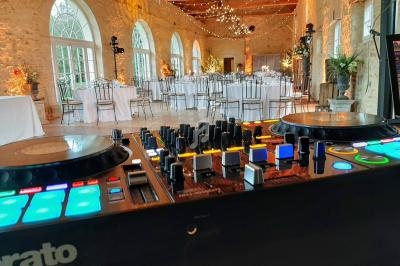 Vue d'une salle de réception élégante avec tables dressées, éclairages suspendus et une table de mixage au premier plan.