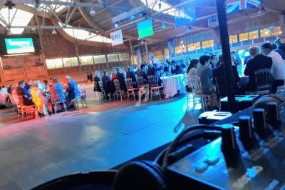 Salle de réception avec des invités assis à des tables rondes, éclairage bleu et drapeaux suspendus.
