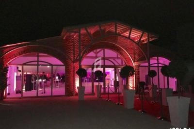 Façade d'une salle de réception éclairée en rose, avec tapis rouge et poteaux de guidage à l'entrée.
