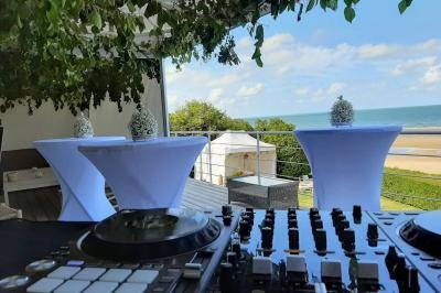 Vue d'une table de mixage en extérieur avec des tables hautes décorées, donnant sur une plage et un ciel dégagé.