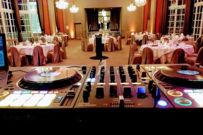 Platines de DJ en premier plan dans une salle élégante avec tables dressées et lustres suspendus.