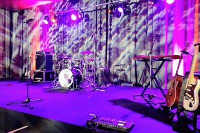 Scène de concert avec batterie, guitares, claviers et micros sous des éclairages colorés.