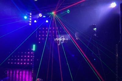 Jeux de lumières colorées et lasers projetés dans une salle sombre avec un écran affichant ’100% DJ’.