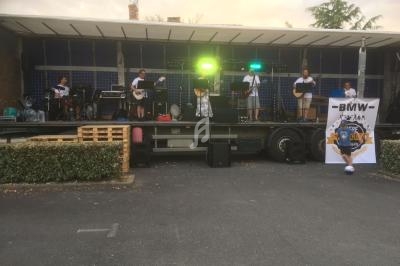 Un groupe de musiciens joue sur une scène extérieure montée sur un camion, avec des instruments et des éclairages colorés.