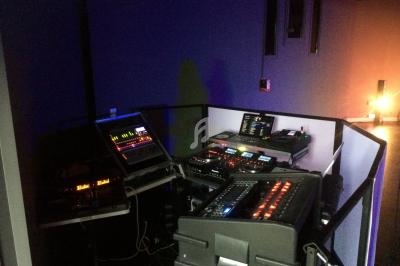 Poste de contrôle audio et lumière dans une salle sombre, équipé de consoles, écrans et équipements techniques.