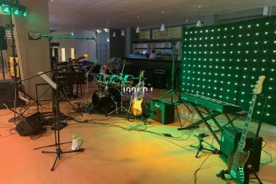 Scène de concert avec batterie, guitares, clavier, micros et éclairage vert en arrière-plan.