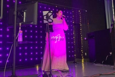 Une chanteuse en robe rose se produit sur scène, éclairée par des lumières violettes, avec un micro à la main.