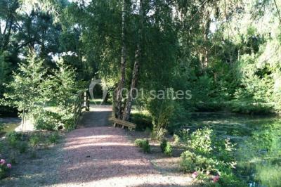 Vue d'un étang entouré d'arbres et de végétation sous un ciel partiellement nuageux.