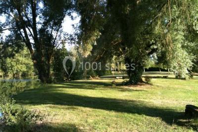 Vue d'un étang entouré d'arbres et de végétation sous un ciel partiellement nuageux.