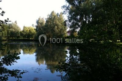 Vue d'un étang entouré d'arbres et de végétation sous un ciel partiellement nuageux.