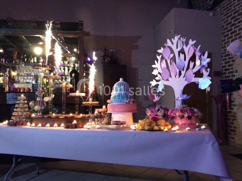 Table décorée pour une fête avec gâteau, bougies, arbre décoratif et fontaines lumineuses en arrière-plan.