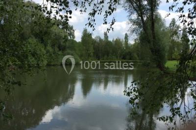 Vue d'un étang entouré d'arbres et de végétation sous un ciel partiellement nuageux.