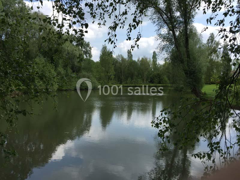 Vue d'un étang entouré d'arbres et de végétation sous un ciel partiellement nuageux.