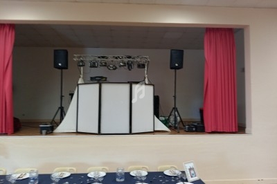 Scène avec équipement de sonorisation et éclairage, vue depuis une salle décorée pour un repas avec tables dressées.