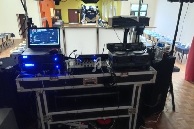 Équipement de DJ installé dans une salle, avec platines, ordinateur, câbles et éclairages en arrière-plan.