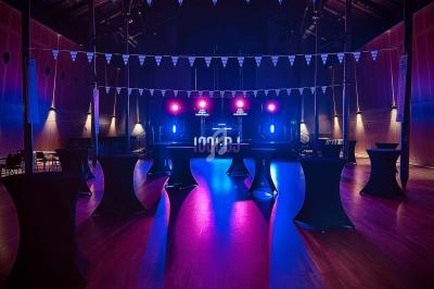 Salle de réception avec éclairage coloré, tables hautes noires et guirlandes triangulaires suspendues.