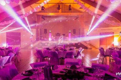 Salle de réception décorée avec des tables dressées et éclairages colorés, ambiance festive et lumineuse.