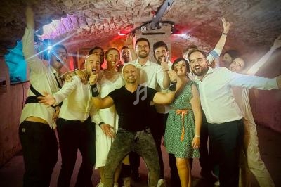 Un groupe de personnes souriantes posant dans un espace voûté en pierre avec un éclairage coloré.