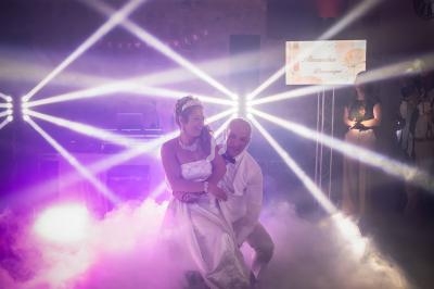 Un couple danse dans une ambiance festive avec des faisceaux lumineux et de la fumée sur la piste.