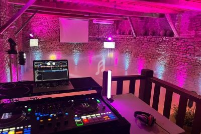 Salle en pierre éclairée de lumières roses avec une console DJ en premier plan et un écran en fond.